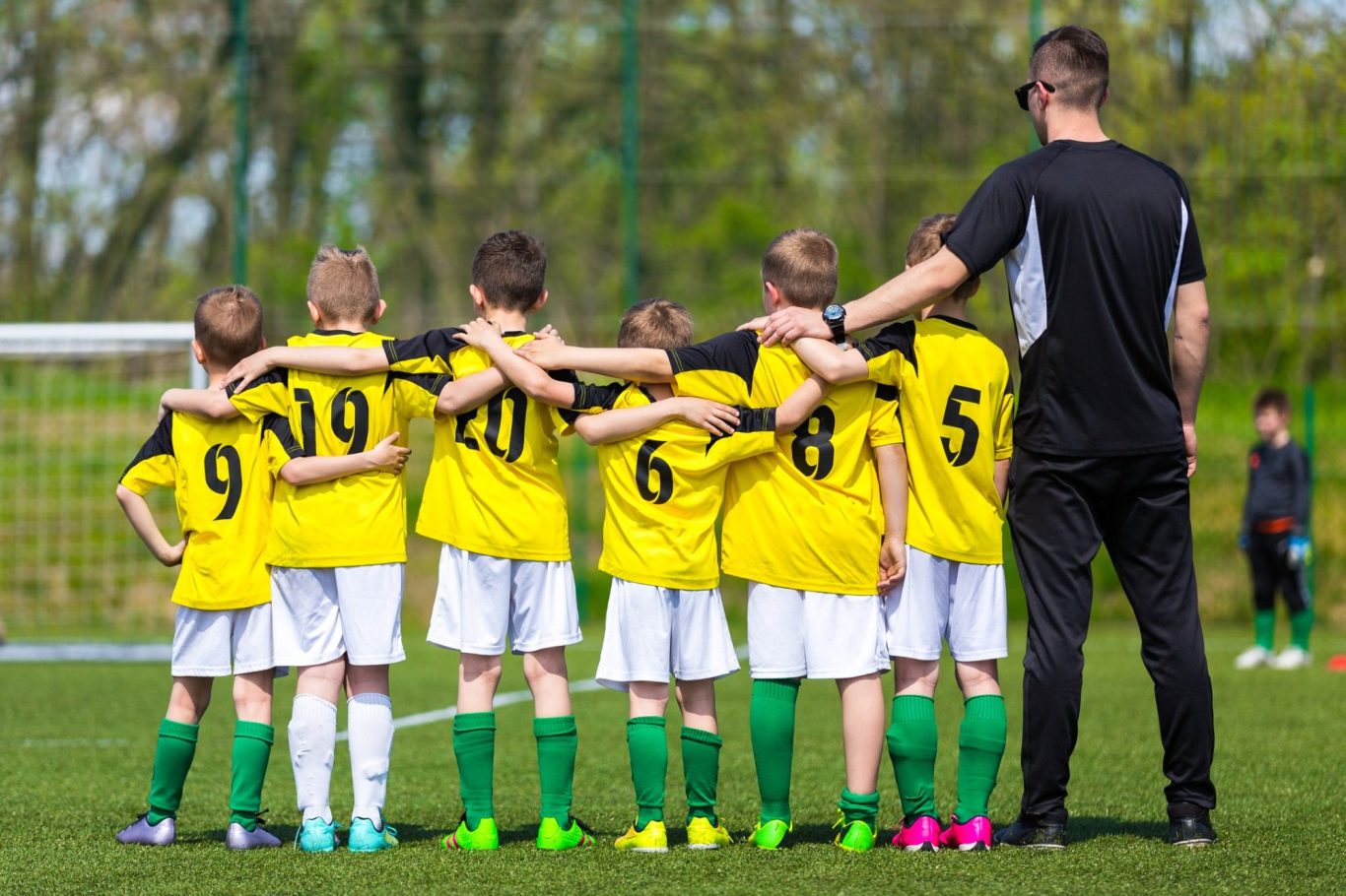 A boys team lined up, arms linked, with their backs to the camera.